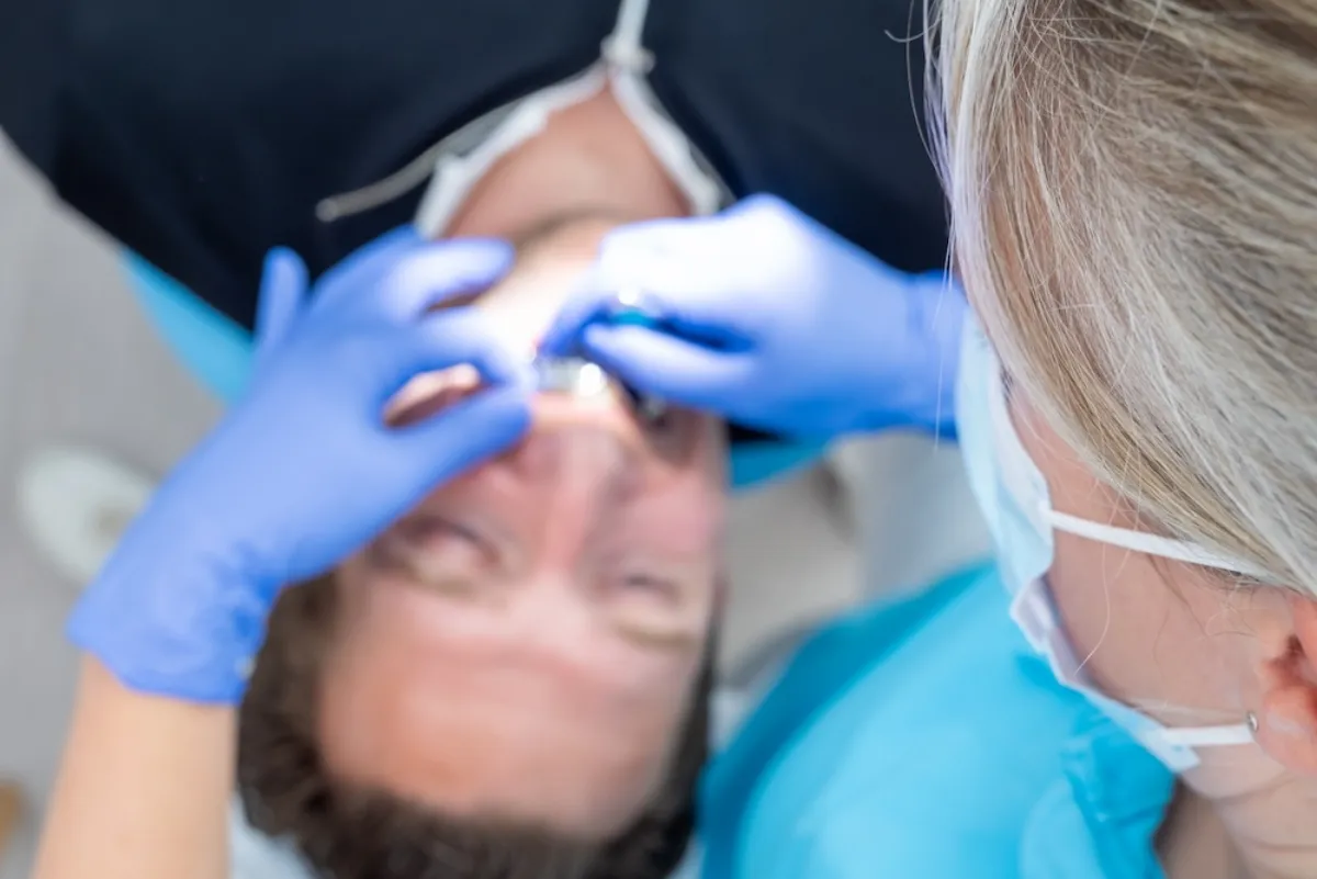 Tandartsassistente met blauwe handschoenen werkt bij een patiënt in de stoel.